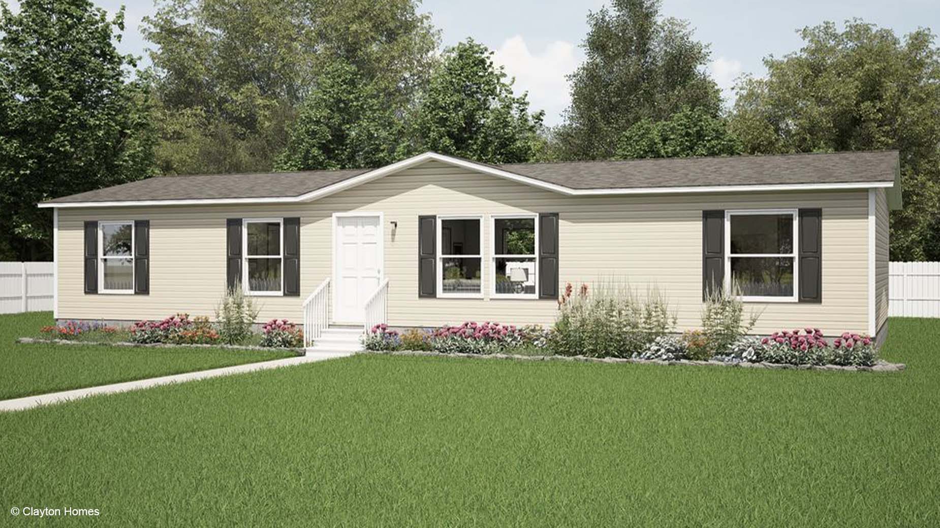A beige ranch-style manufactured home with a white door, shutters, and a garden in front, surrounded by a green lawn.