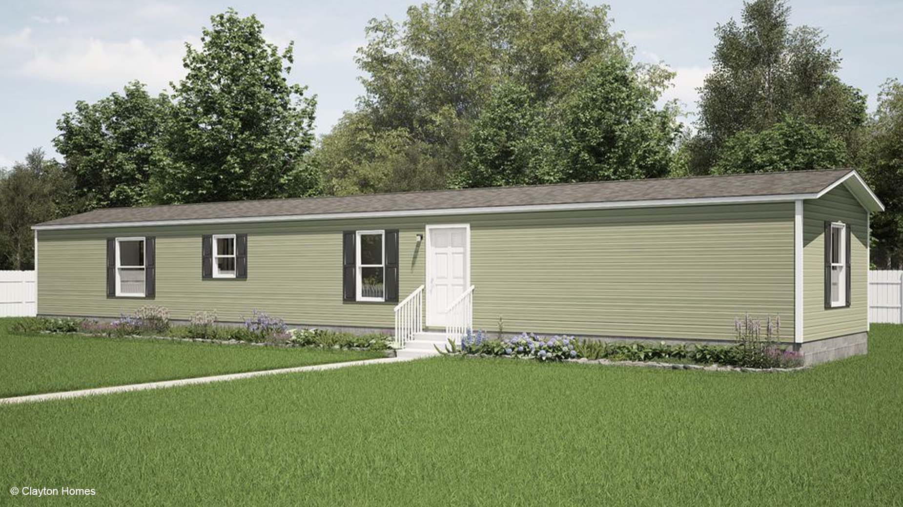 Charming single-story manufactured home with white trim, central steps, and a grassy yard bordered by trees in the background.