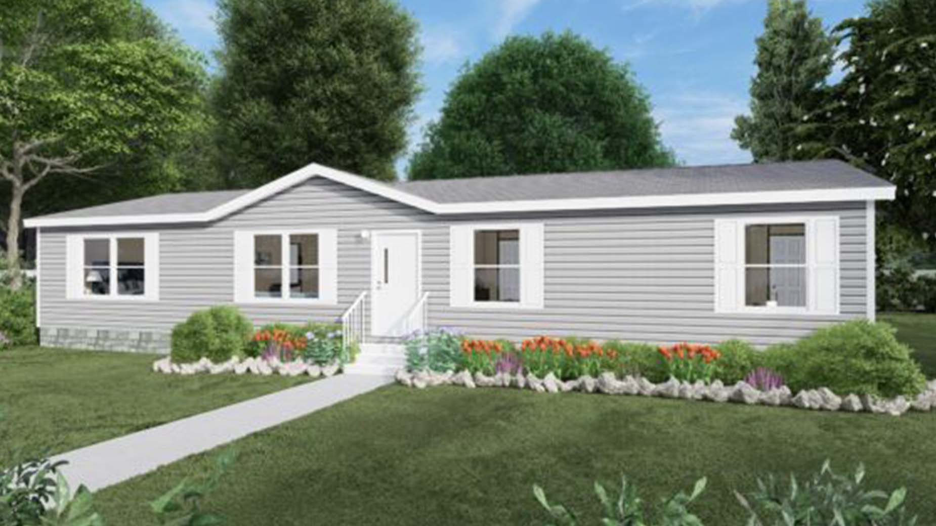 Single-story gray manufactured home with white trim, surrounded by a green lawn, trees, and colorful flower beds.