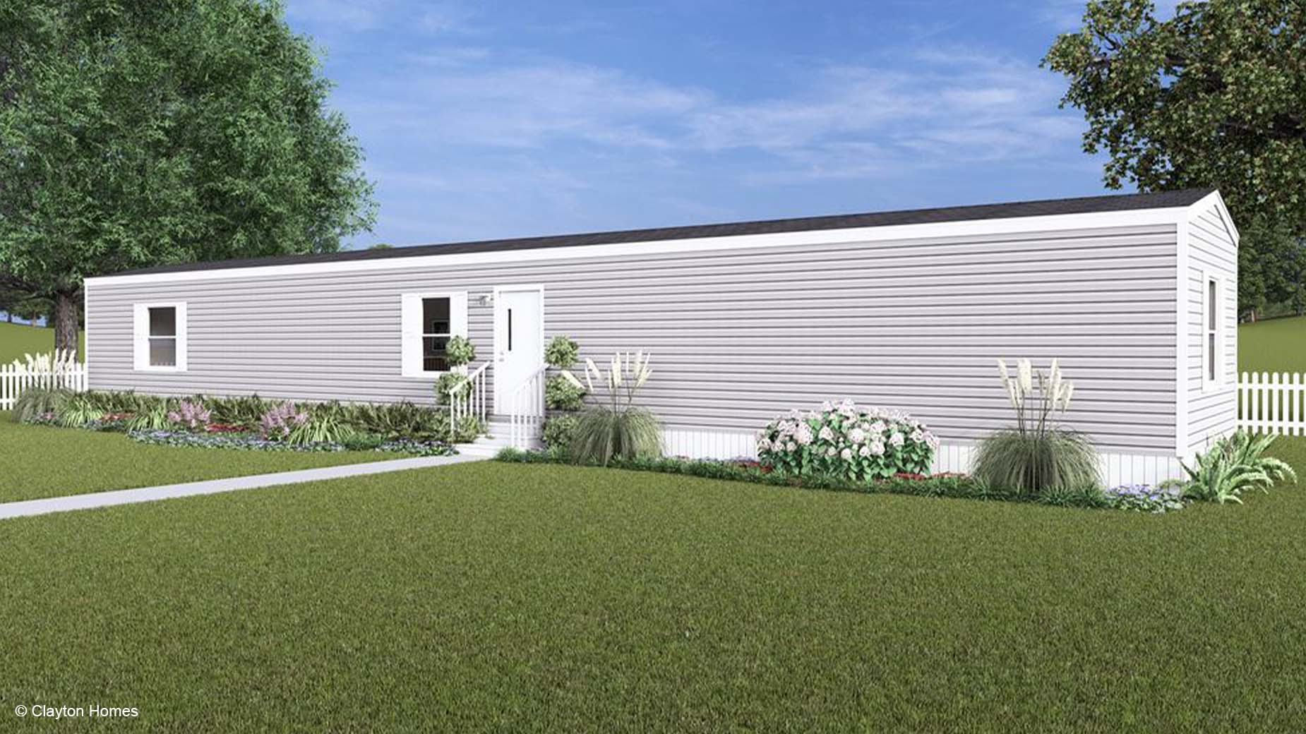 A long, single-story gray manufactured home with white trim, a small garden, and a charming white picket fence.