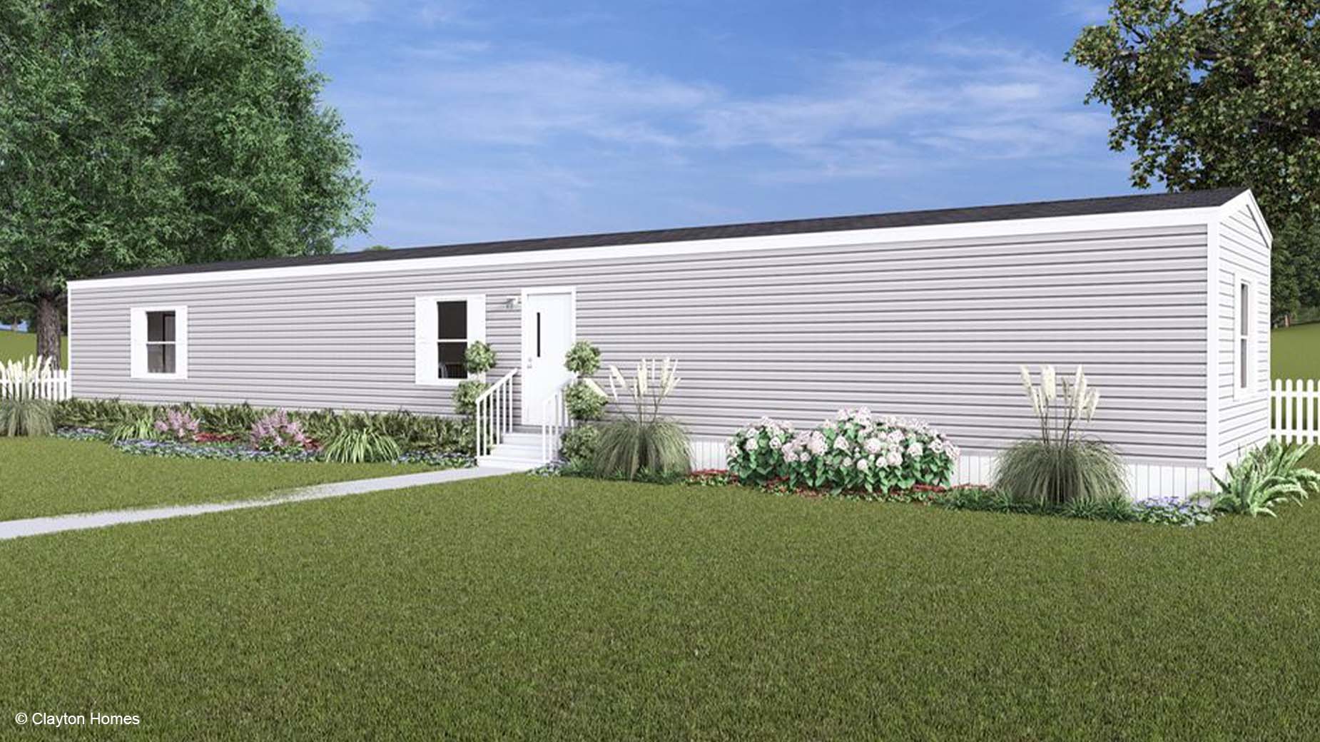 A long, light gray manufactured home with white trim, surrounded by green lawn and landscaping.