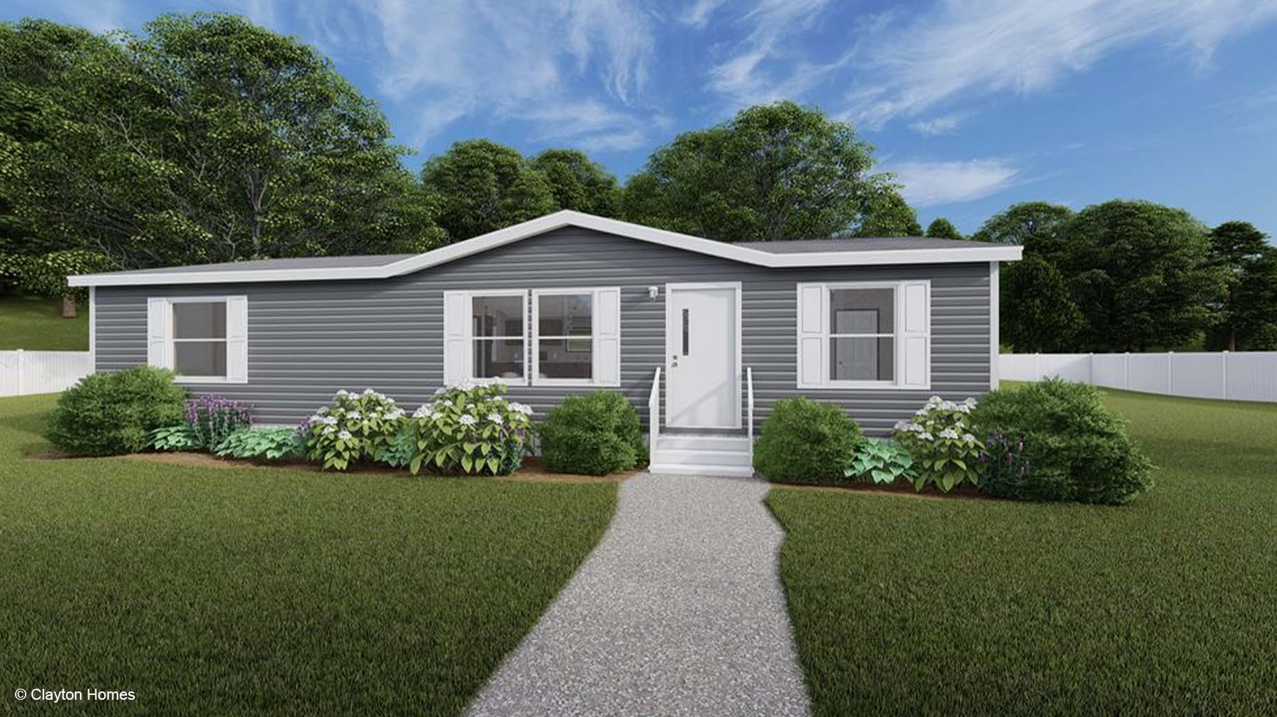 A gray manufactured home with white trim, front steps, and landscaped bushes sits in a grassy yard.
