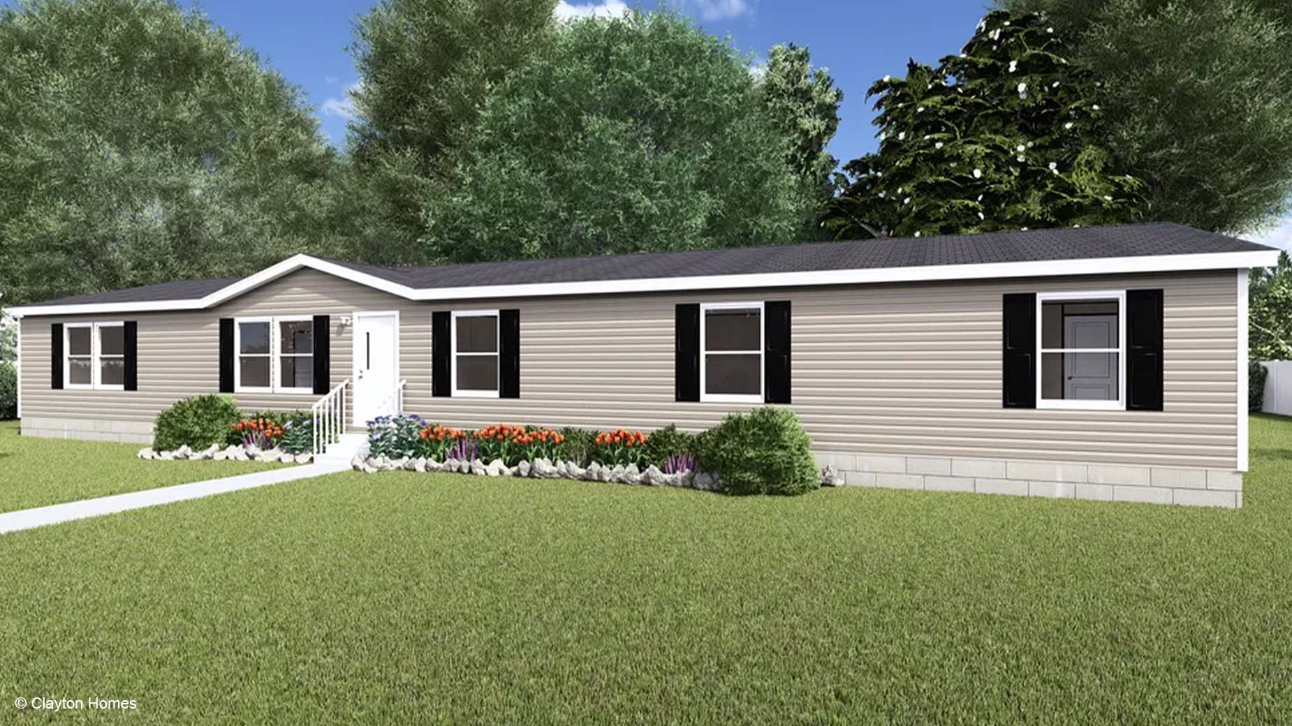A beige manufactured home with black shutters, white trim, and a beautifully landscaped front yard filled with flowers and shrubs.